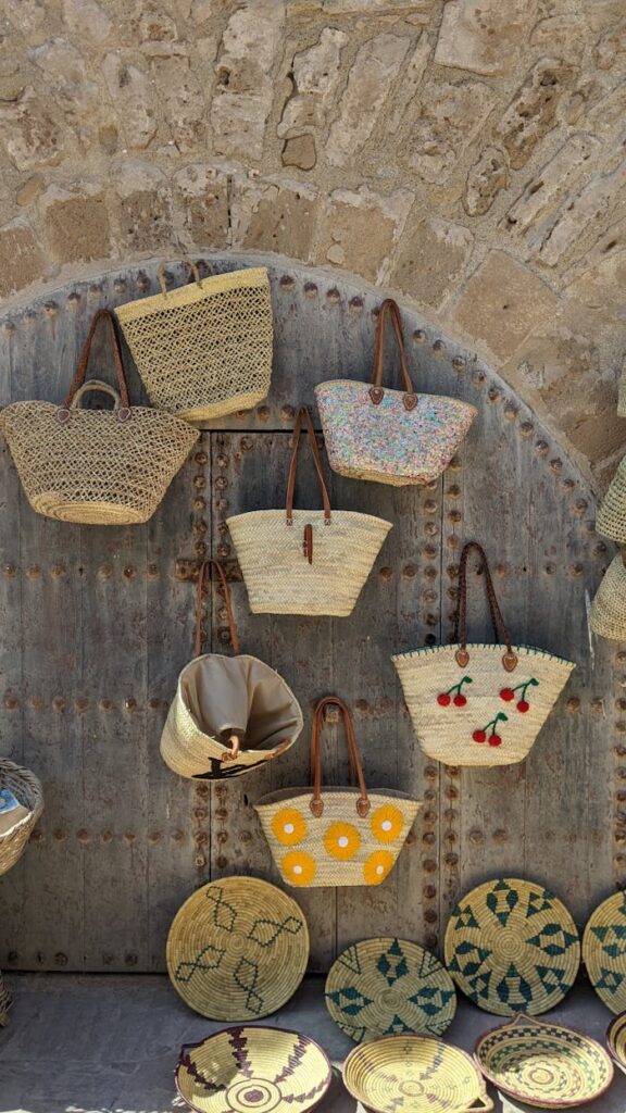 A display of handcrafted straw bags on a rustic stone wall in Essaouira, Morocco.